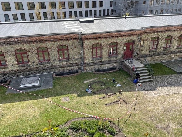 Das Bild zeigt die Baustellensituation, mit dem ausgegrabenen Wortteil CHT von oben fotografiert. Im Hintergrund ist das Gebäude zu sehen auf dessen Dach das Wort AUF steht.