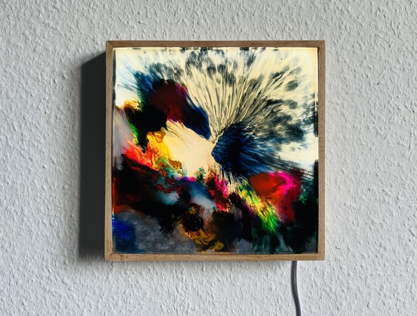 Das Bild zeigt einen rahmenartigen Kasten aus Holz mit Kabel. Vorne ist ein sehr buntes abstraktes Bild eingelassen, das hinterleuchtet ist und an eine Unterwasserszene erinnert. 