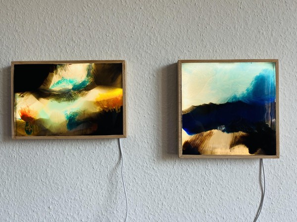 Das Bild zeigt zwei rahmenartige Kästen aus Holz mit Kabeln. Vorne ist jeweils ein abstraktes Bild eingelassen. Beide Bilder sind hinterleuchtet und erinnern an Szenen unter dem Meer.